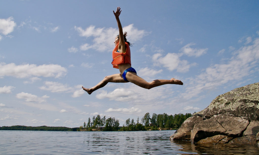 Girl cliff jumping in the boundary waters into water with a life jacket